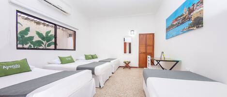 A hotel room with two beds, a small table, a chair, a painting, and an air conditioning unit.
