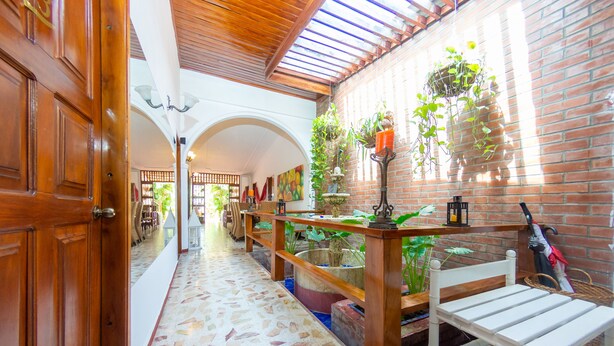 Un pasillo con suelo de baldosas, bancos de madera y plantas colgantes.