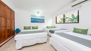 Habitación de hotel con tres camas, cada una con almohadillas verdes con la etiqueta "Ayenda Hotels".