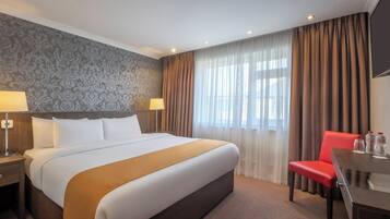 A hotel room with a large bed, a desk, a chair, and a window with curtains.