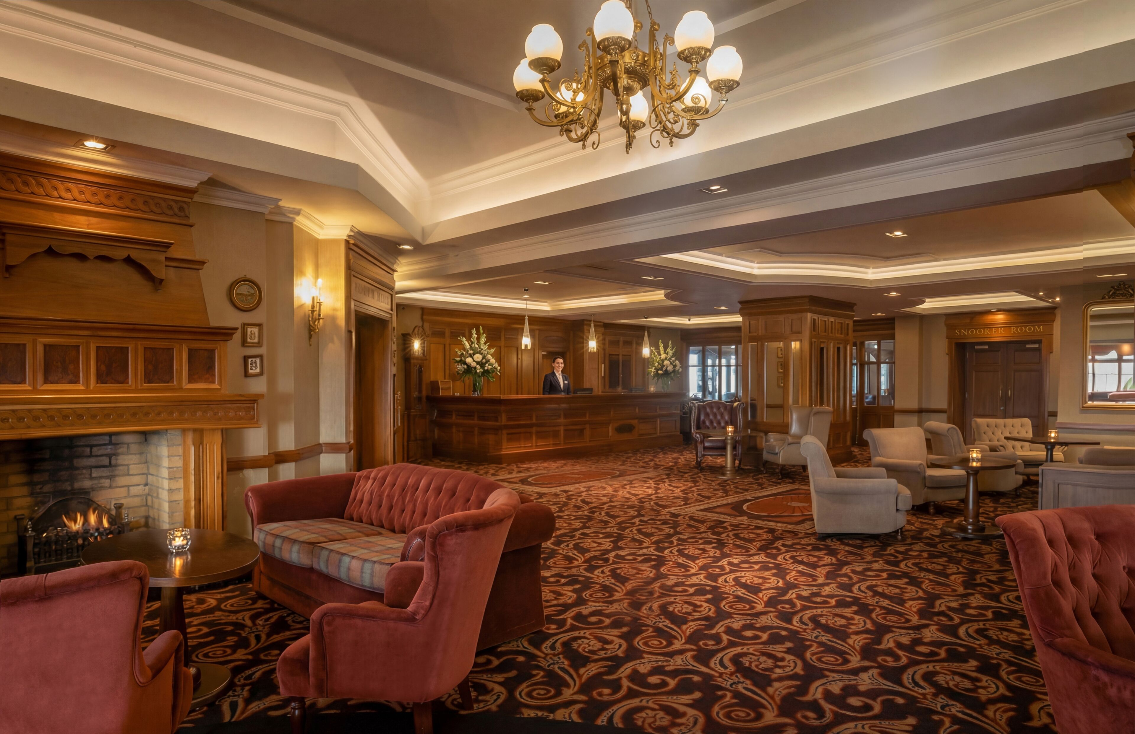 A spacious lobby with a fireplace, plush seating, a reception desk, and a chandelier.