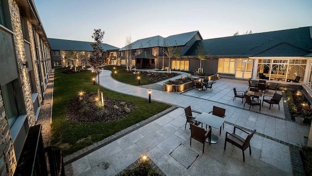 Un patio con mobiliario exterior, un sendero sinuoso y un edificio con grandes ventanales.