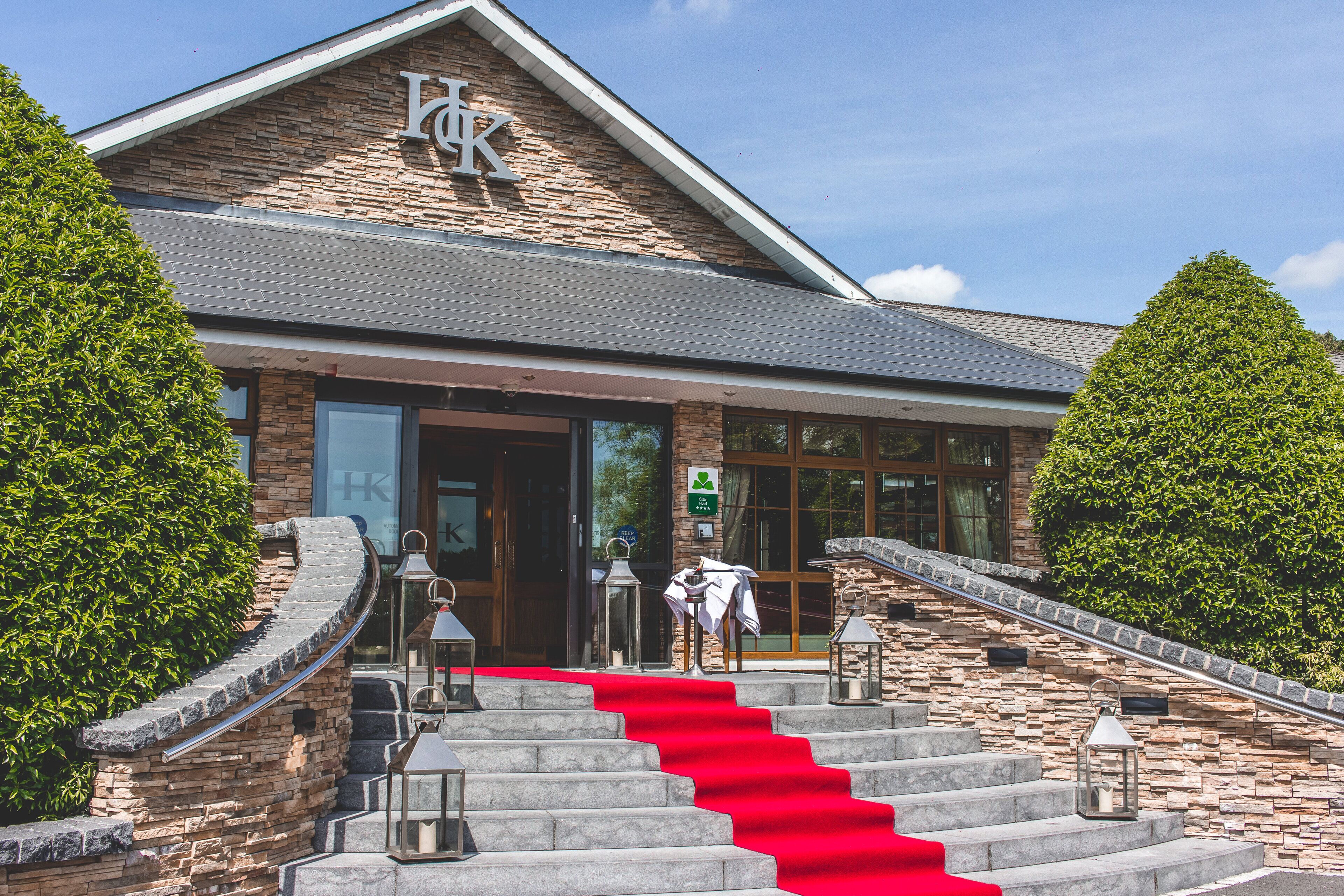 A hotel entrance with stone steps, a red carpet, and a sign with a 'K' logo.