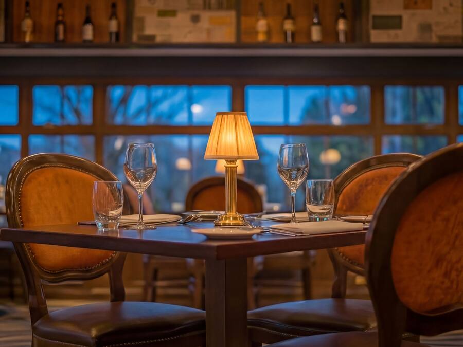 L’intérieur d’un restaurant, avec une table dressée pour quatre personnes, comprenant des verres à vin et une lampe.
