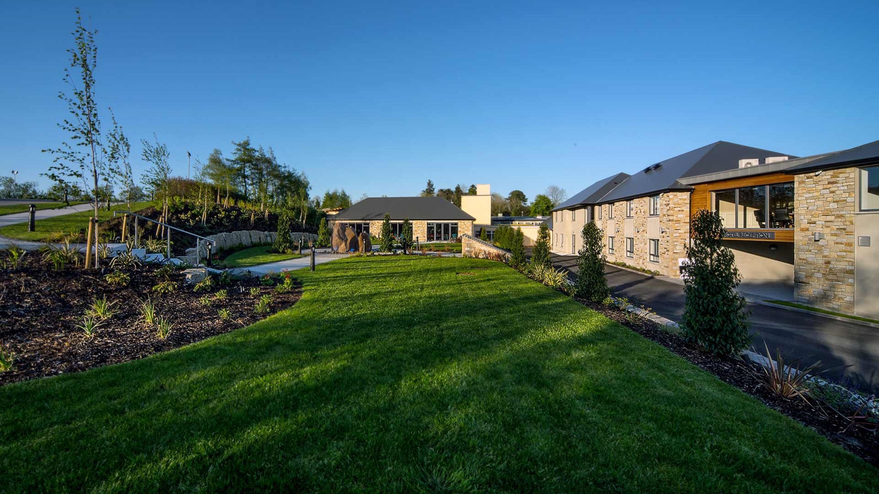 A modern hotel with a stone facade, a well-maintained lawn, and a clear sky.
