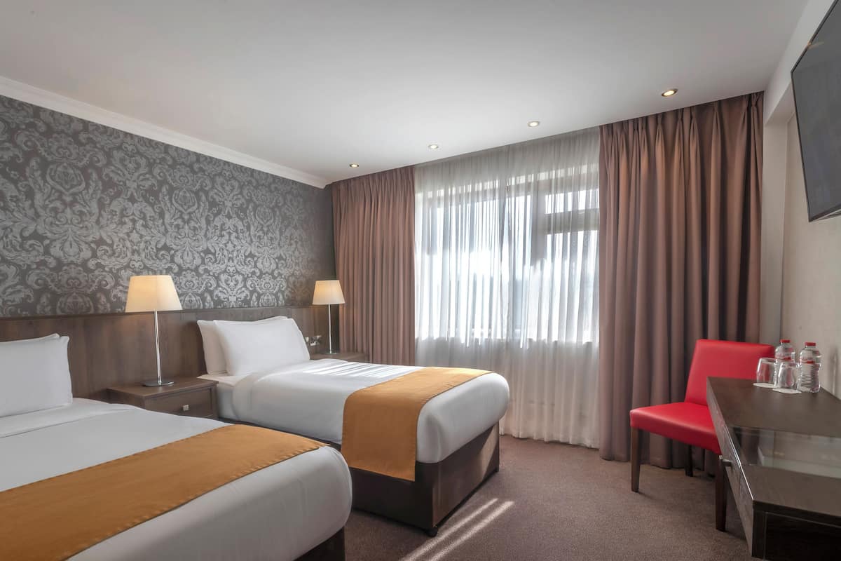 A hotel room with two beds, a desk, a chair, and a large window with curtains.