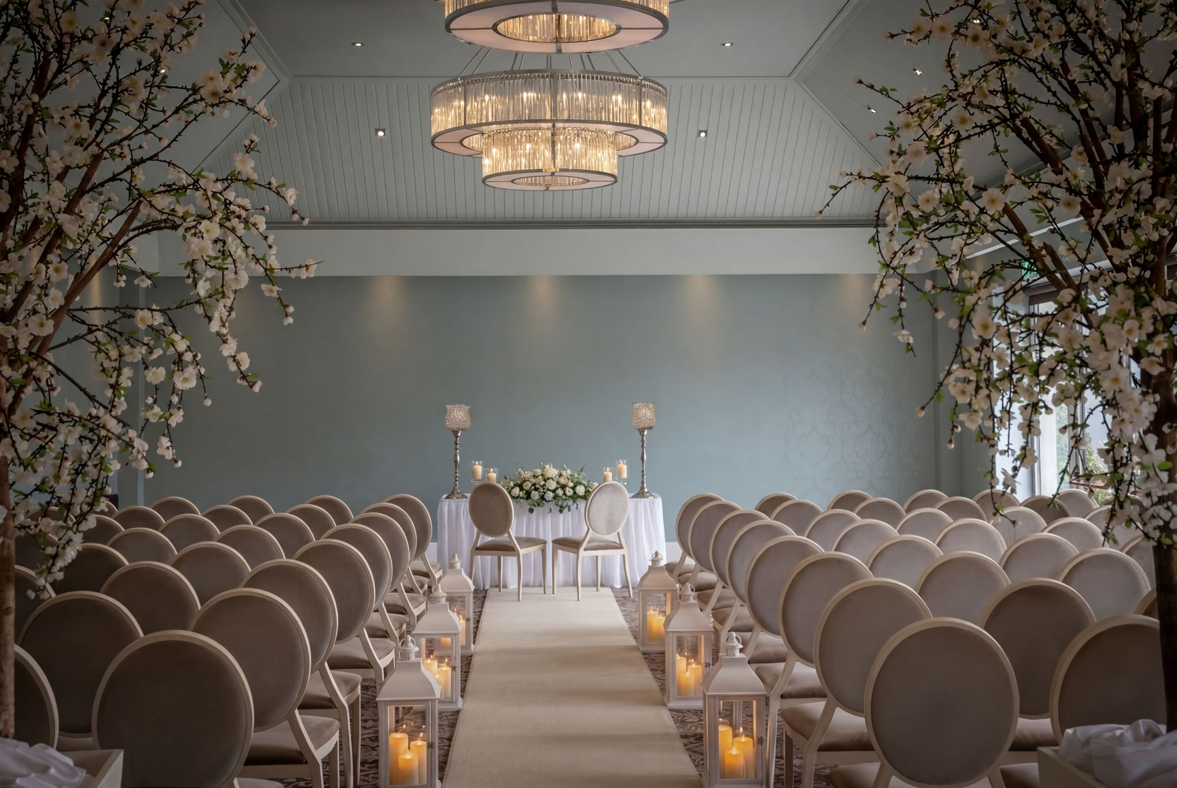 A row of chairs facing a table with a floral arrangement, under a chandelier.