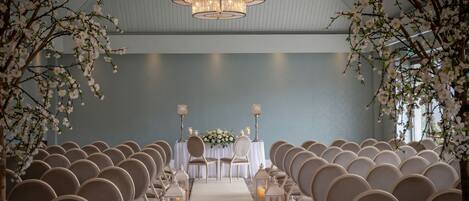 A row of chairs facing a table with a floral arrangement, under a chandelier.