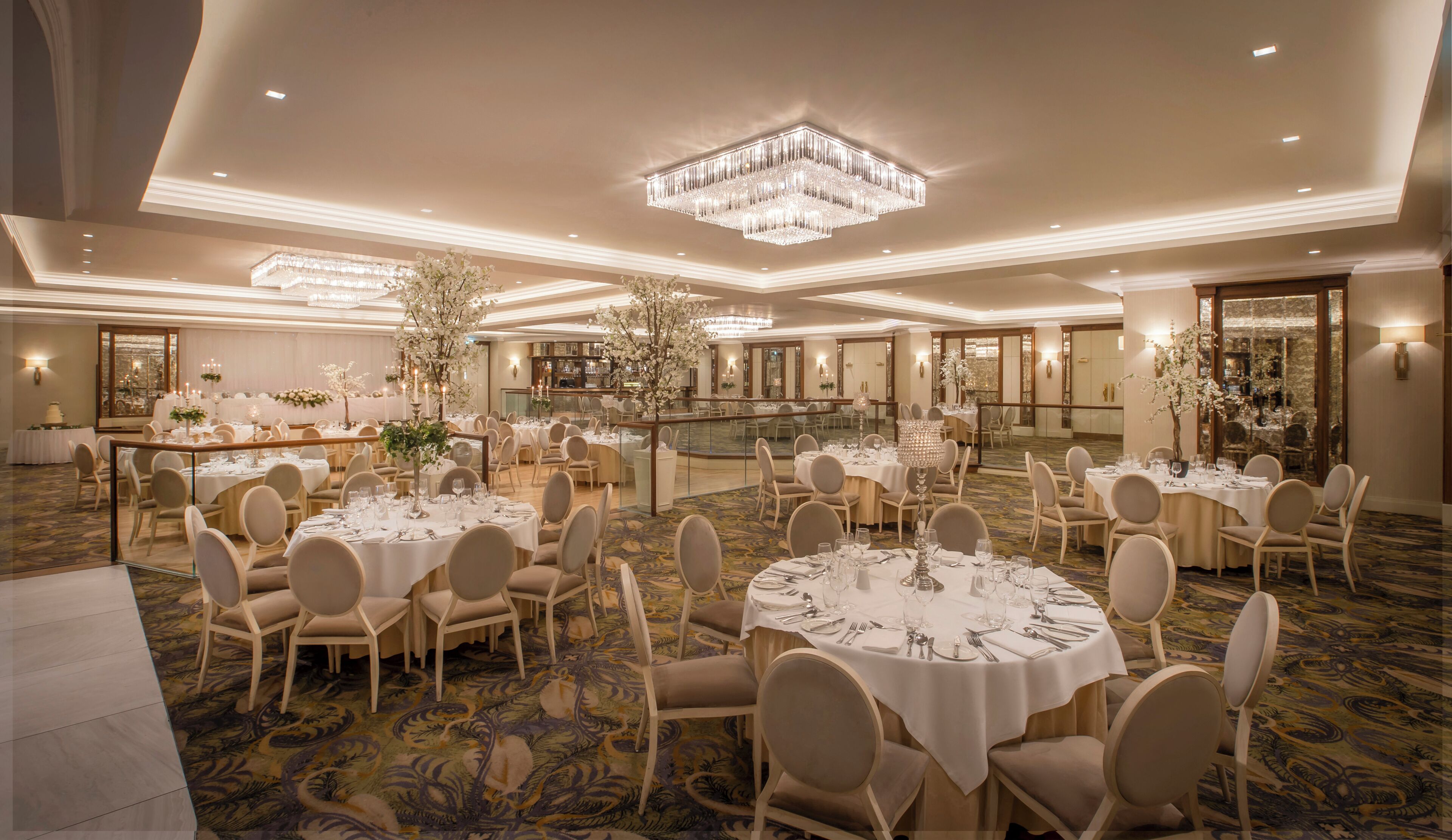 Un amplio salón de banquetes con mesas redondas, sillas, candelabros y centros de mesa florales.