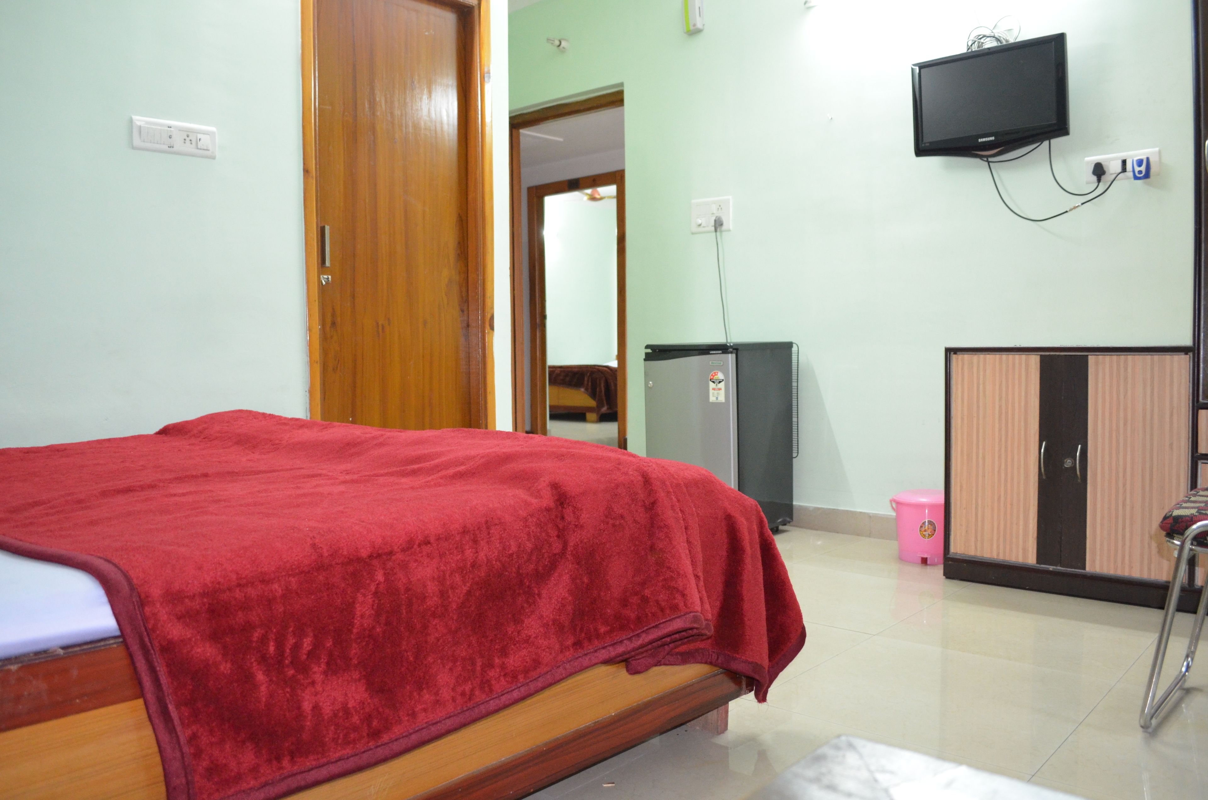 A room with a bed, a television mounted on the wall, a wardrobe, and a small refrigerator.