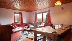 Un salon chaleureux avec un plafond en bois, des canapés rouges, une table à manger en bois et de grandes fenêtres avec des rideaux.