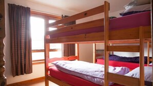 Een slaapkamer met stapelbed, raam, gordijnen en een houten hoofdbord.
