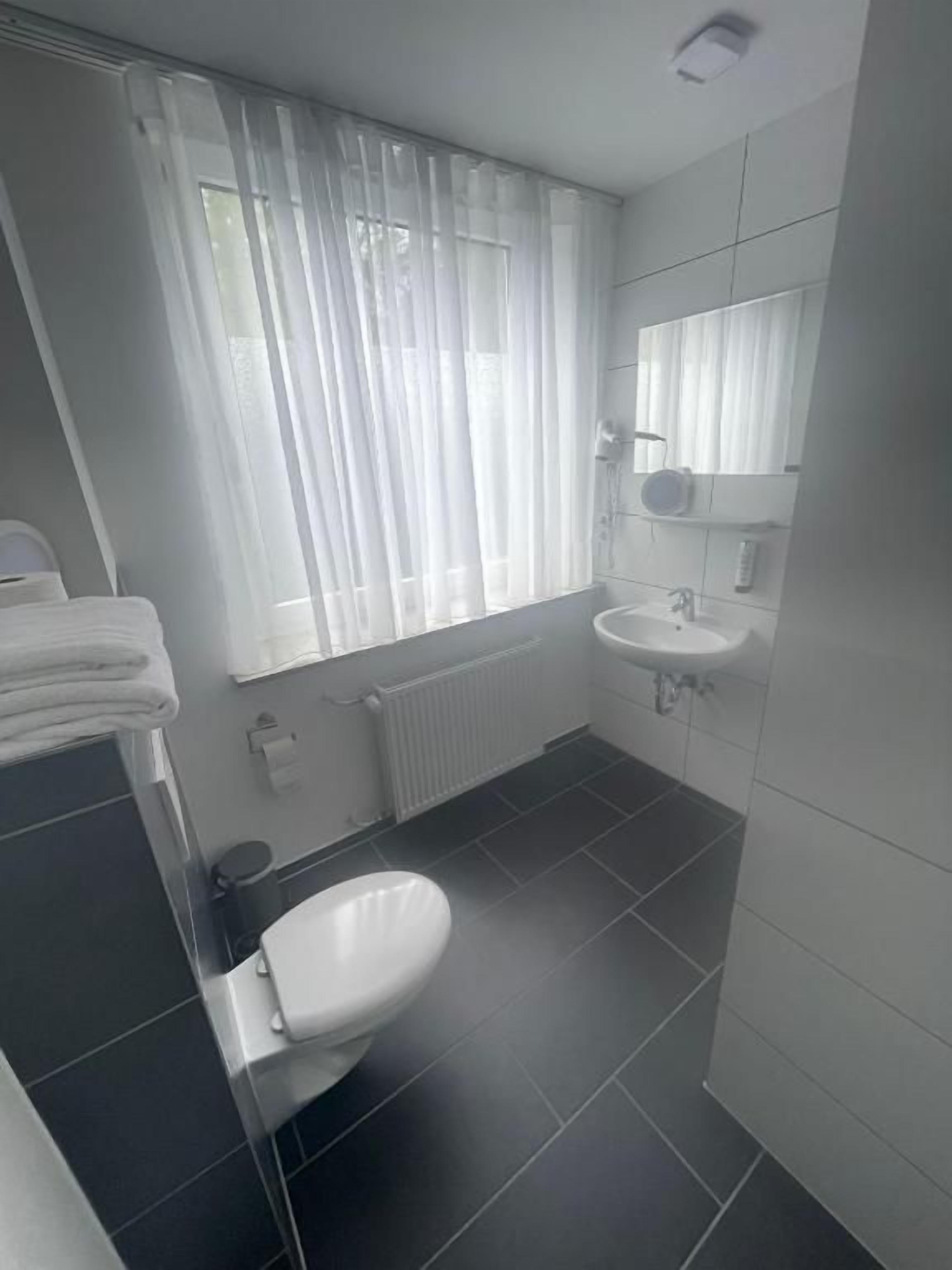 Ein Badezimmer mit Toilette, Waschbecken und einem fenster mit Vorhängen.