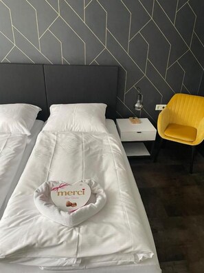 A hotel room with two beds, a bedside table with a lamp, and a yellow chair. - MOTELO Bielefeld (Bielefeld)