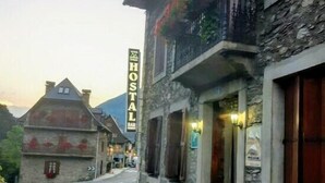 Un bâtiment en pierre avec une enseigne indiquant « HOSTAL » et un balcon orné de fleurs rouges.