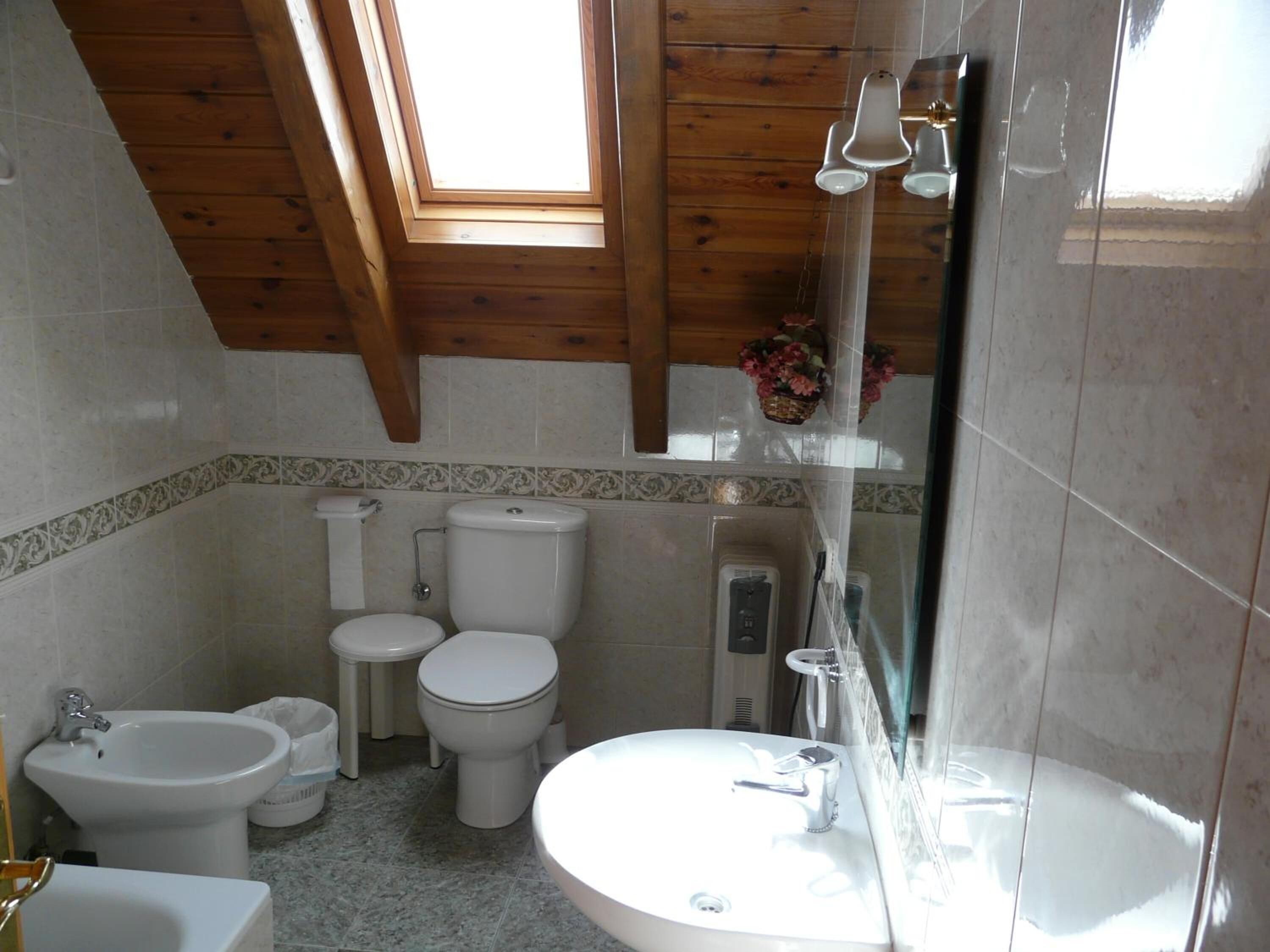 Un baño con tragaluz, dos inodoros, un bidé, un lavabo y una ducha.