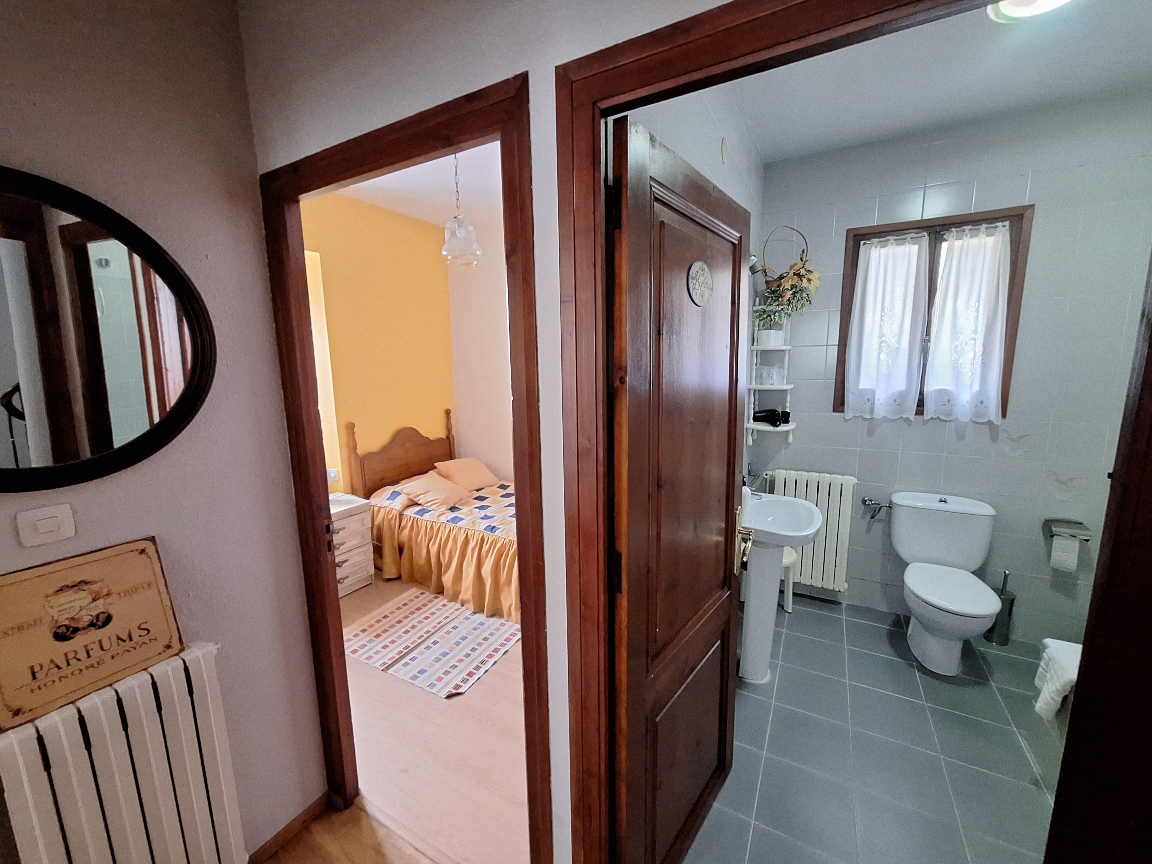 Une chambre avec un lit, une porte en bois et une salle de bain comprenant des toilettes, un lavabo et un radiateur.