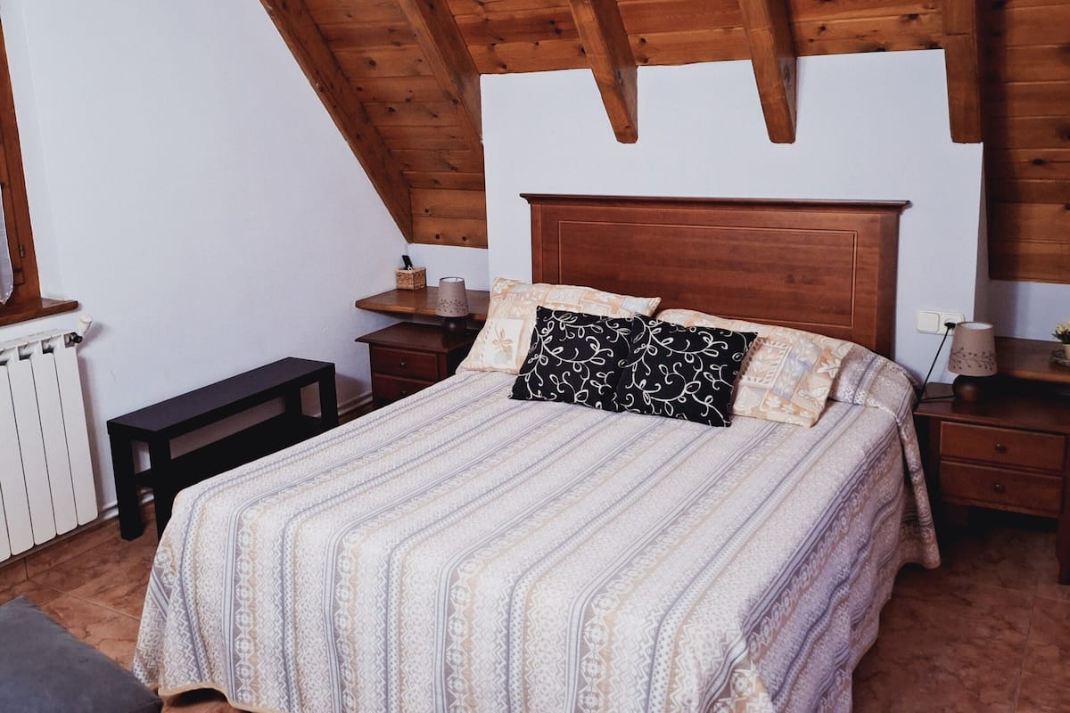 Ein Schlafzimmer mit Holzboden, einem großen Bett mit gemusterten Textilien, einem Nachttisch und einer Bank.