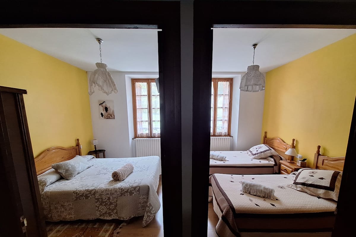 Ein Schlafzimmer mit zwei Betten, einem hölzernen Kopfteil, einem kleinen Nachttisch, einer Lampe und einem Fenster mit Vorhängen.