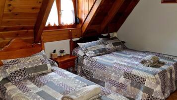 Un dormitorio acogedor en el ático con dos camas, vigas de madera, una ventana con cortinas y una mesita de noche con lámpara.