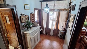 Une pièce avec un plafond en bois, un sol carrelé, une cheminée, un lustre et une fenêtre avec des rideaux.