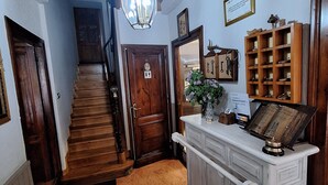 Un escalier en bois menant à un deuxième étage, une console blanche avec un miroir et un porte-chaussures en bois doté de compartiments numérotés.