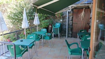Un patio al aire libre con mesas y sillas de plástico verde, un toldo verde y una pared de piedra con plantas.