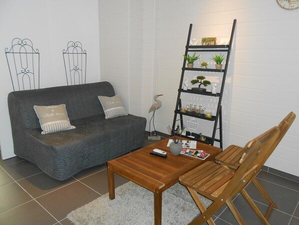 A living room with a grey sofa, a wooden coffee table, and a black bookshelf with decorative items.