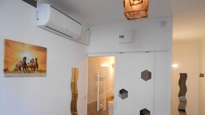 A hallway with a white air conditioning unit, a painting of horses, a bathroom with a towel rack, and geometric wall decorations. - B&B La Maison d'Olivier (Beaucaire)