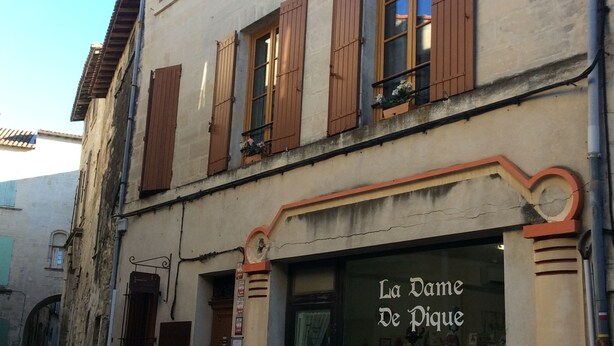 A narrow cobblestone street with a building featuring a shop named "La Dame De Pique". - B&B La Maison d'Olivier (Beaucaire)