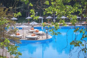 Un espace piscine agrémenté de chaises longues et de parasols, entouré d’arbres.