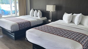 A hotel room with two beds, a nightstand, a lamp, and a view of the outside. - Lake Erie Lodge (Erie)