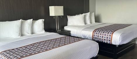 Een hotelkamer met twee bedden, een nachtkastje met een lamp en een plafondarmatuur.