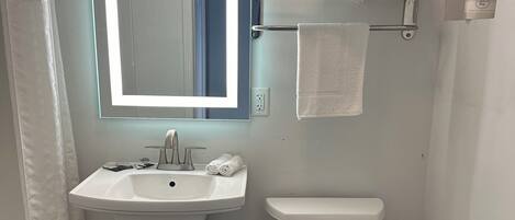 A bathroom with a white sink, a toilet, and a mirror with a light. There are towels on a rack and a shower curtain.