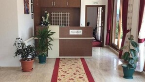 A reception area with a reception desk labeled "Reception," a chandelier, potted plants, and a patterned carpet. - Hasdikoz Abdik Hotel (Of)
