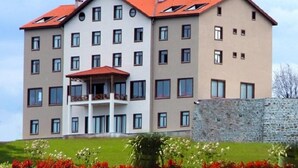 A multi-story hotel with a red roof, balconies, and a stone wall in the foreground. - Hasdikoz Abdik Hotel (Of)
