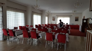 A dining hall with red chairs and white tablecloths, chandeliers, and a waiter. - Hasdikoz Abdik Hotel (Of)