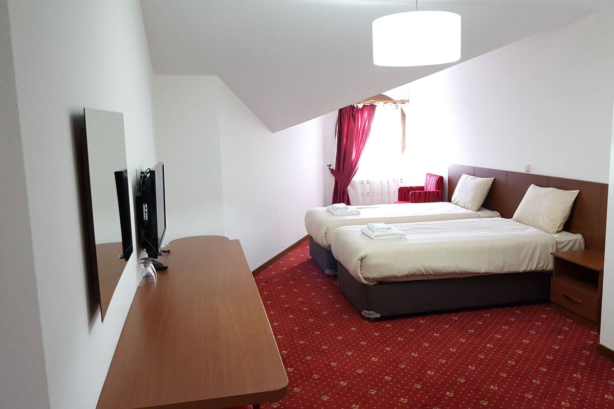 A hotel room with a bed, a desk, a TV, and a window with curtains.