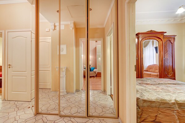 Relax in a spacious room with a comfortable bed, sofa, and chair, surrounded by a large mirror and stylish furniture.