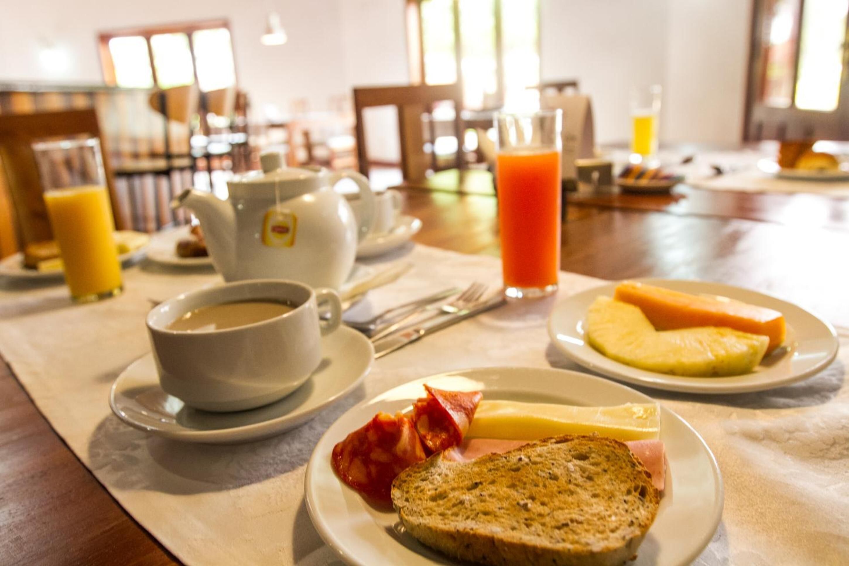 Une table mise pour le petit-déjeuner, avec une nappe pour deux personnes, comprenant des assiettes avec des toasts, des œufs, du bacon et une tasse de café.