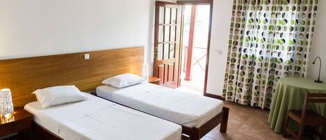Una habitación con dos camas individuales, un cabecero de madera, una mesita con mantel verde y una silla.