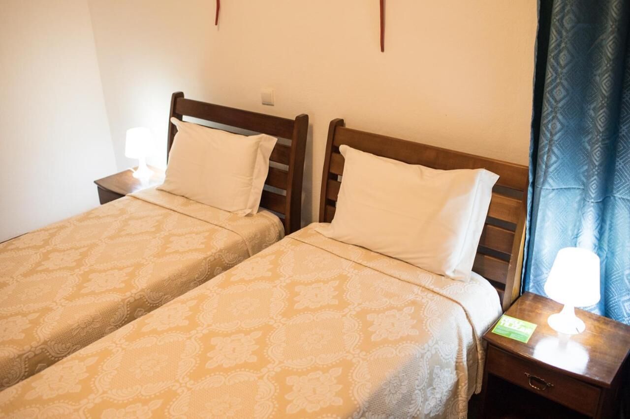 Two single beds with wooden headboards, a nightstand with a lamp, and a blue patterned curtain.