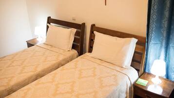 Two single beds with wooden headboards, a nightstand with a lamp, and a blue patterned curtain.