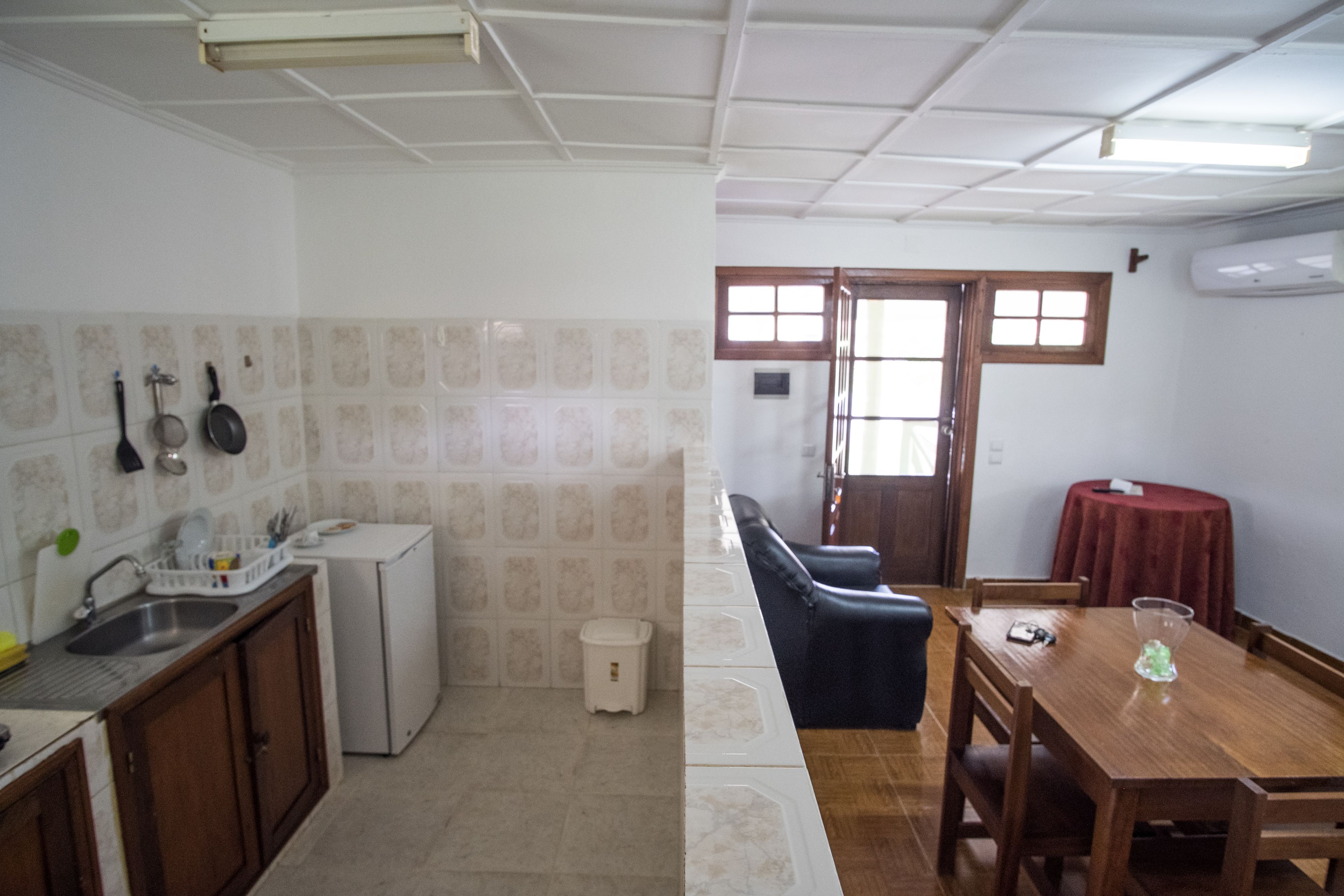 A compact kitchen with a refrigerator, sink, and hanging utensils. A dining area with a wooden table and chairs is visible.