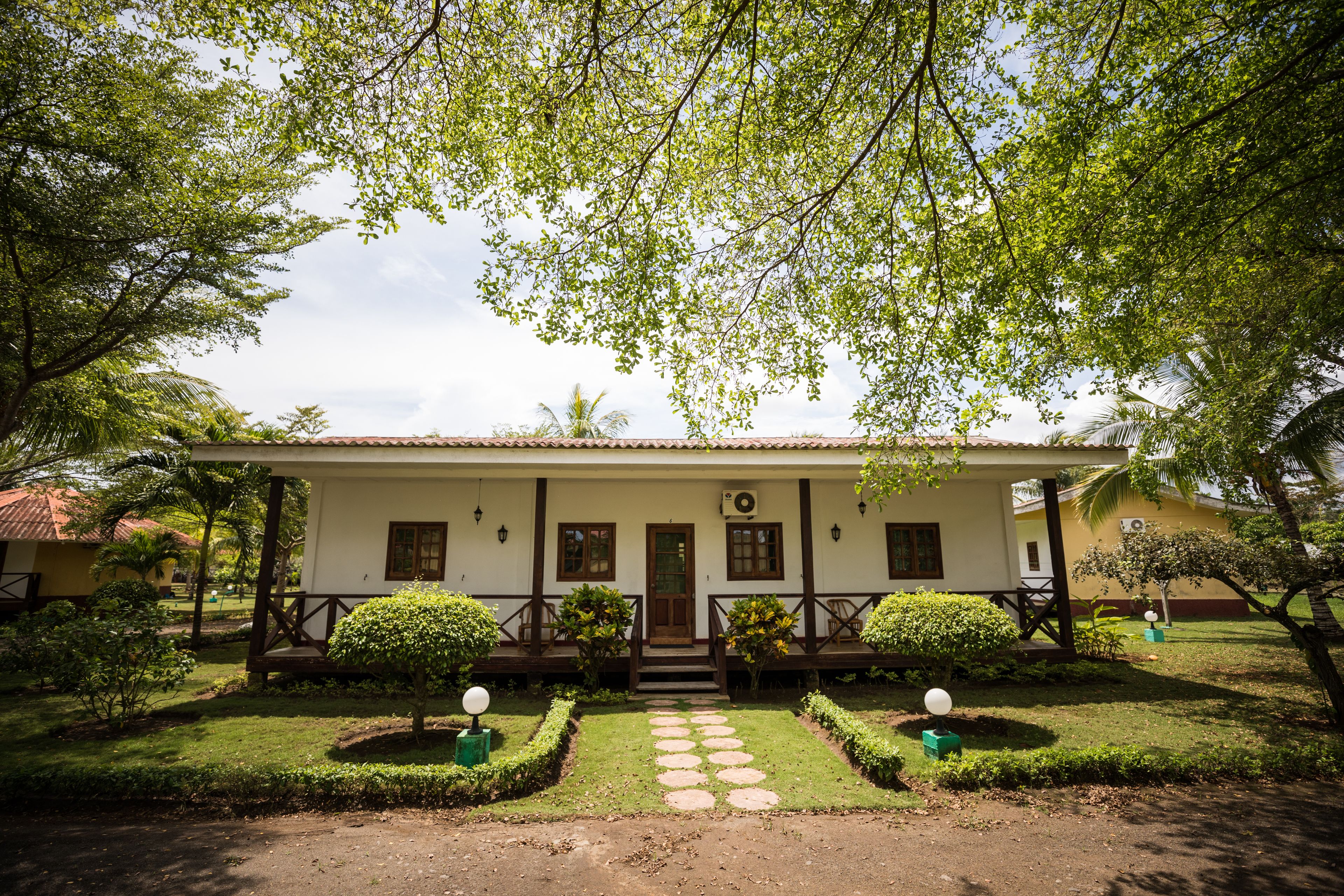 A two-story building with a white facade, a wooden porch, and a well-maintained garden with a stone pathway leading to the entrance.