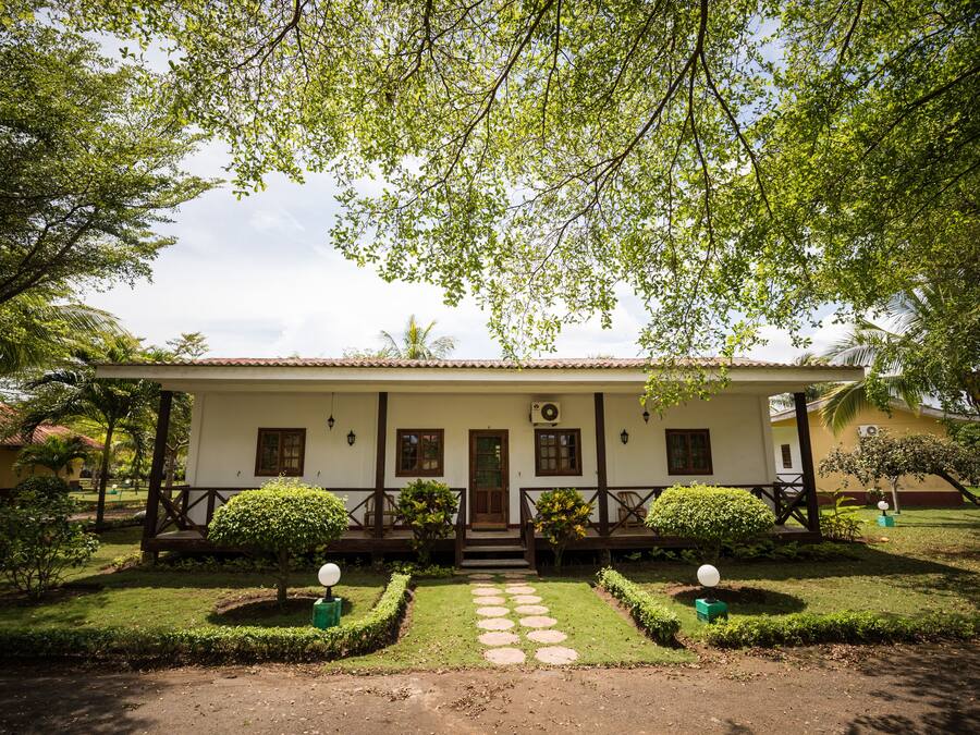 A two-story building with a white facade, a wooden porch, and a well-maintained garden with a stone pathway leading to the entrance.
