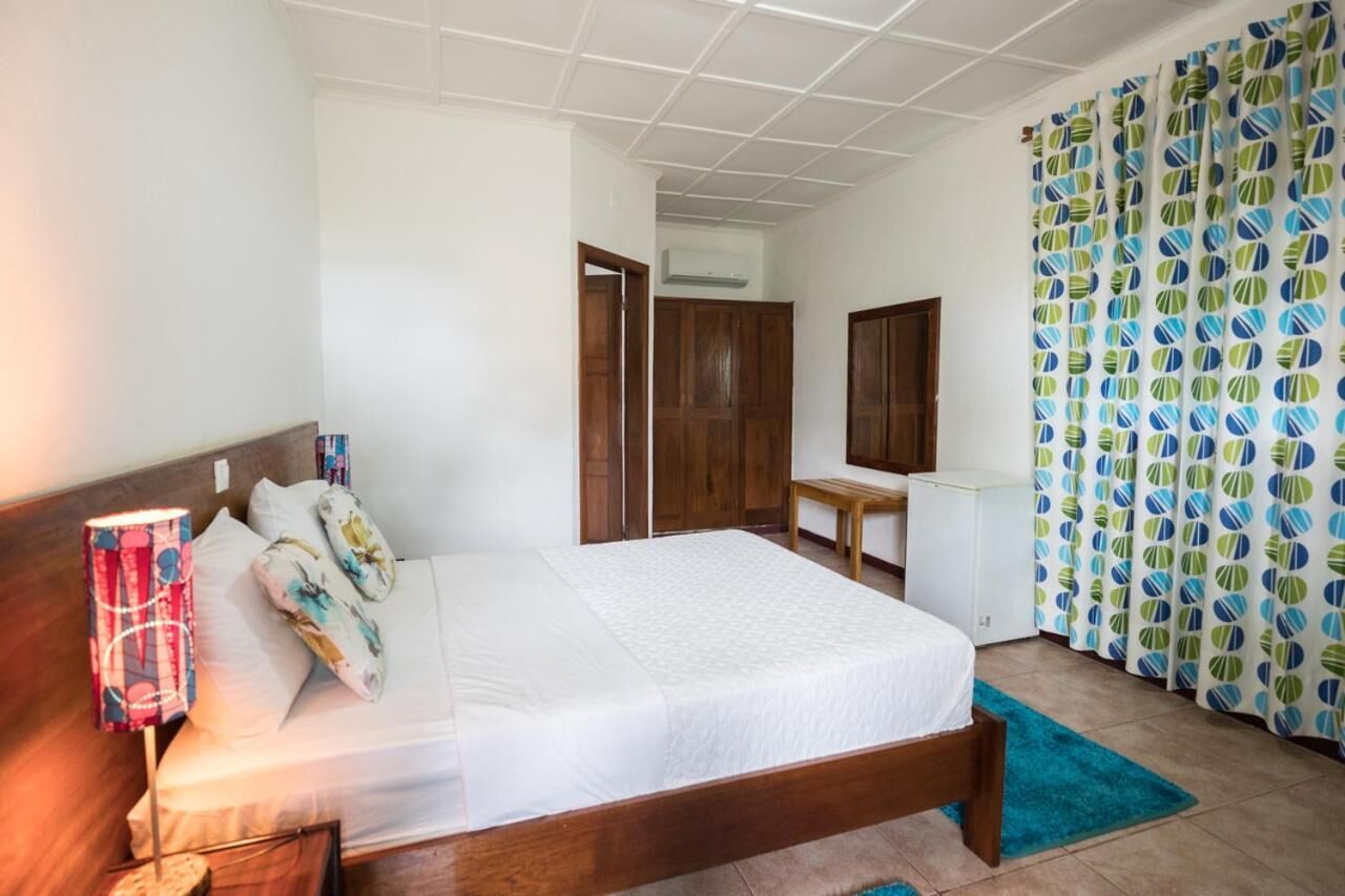 A hotel room with a bed, a desk, a chair, a window with curtains, and a door.