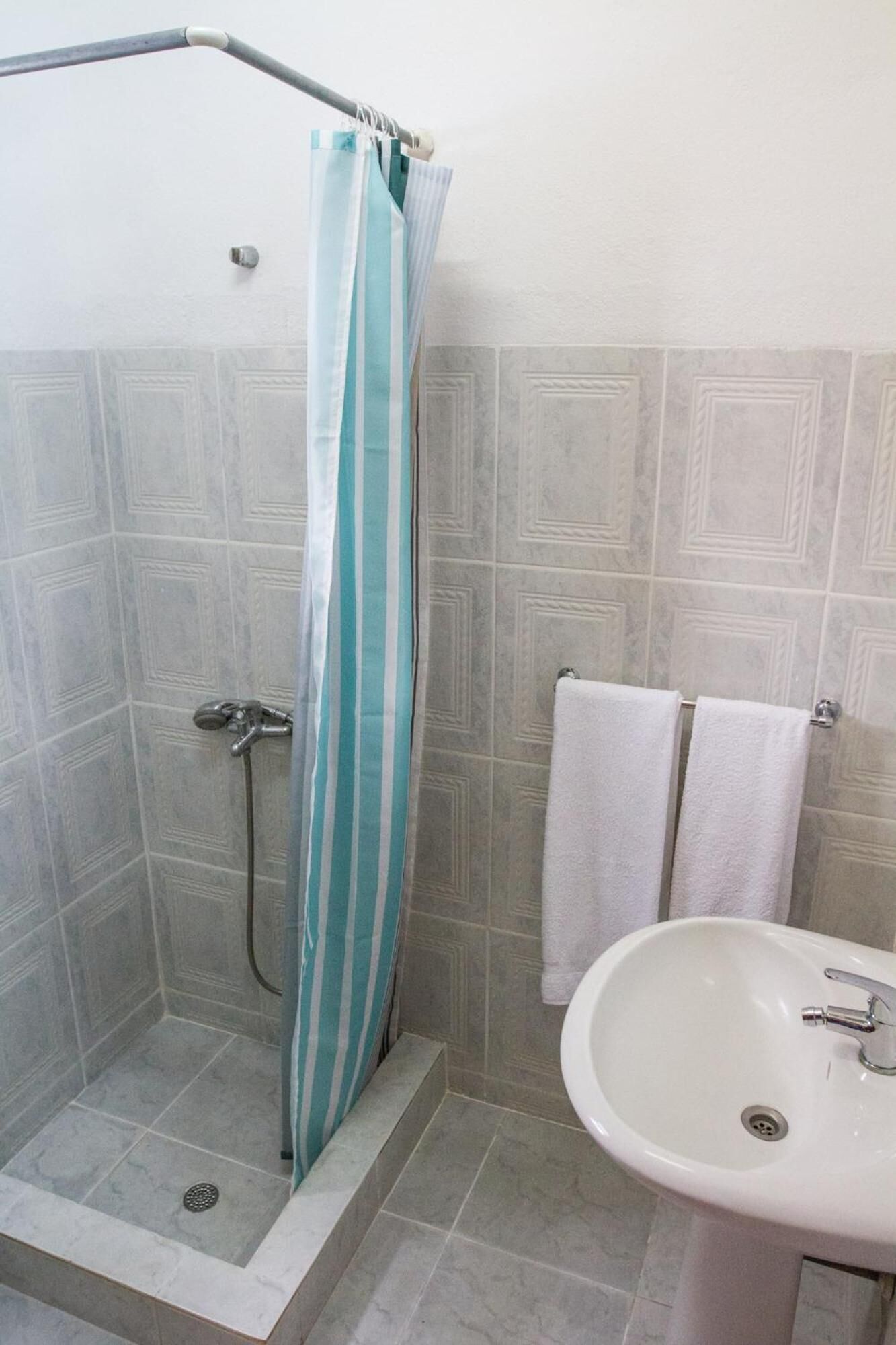Een douche met een gestreept gordijn, een witte wastafel en twee handdoeken aan de muur.