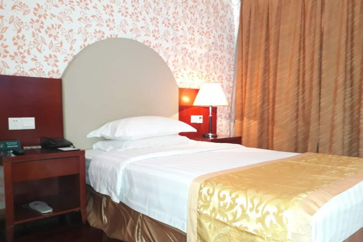 Une chambre d’hôtel avec un lit, une table de chevet, une lampe et un mur recouvert d’un papier peint à motifs floraux.