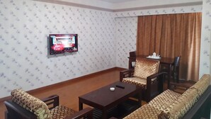 A living room with patterned wallpaper, a television, a sofa, and a coffee table. - Sogecoa Apart Hotel (Maputo)